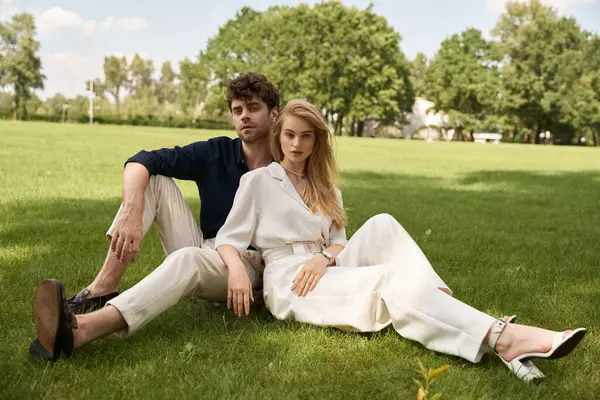 Casal elegante em traje refinado desfrutando de um dia de lazer sentado na grama em um parque exuberante. — Fotografia de Stock