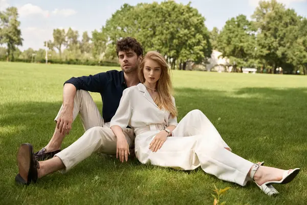 Elegant couple in refined attire enjoying a leisurely day sitting on grass in a lush park. — Stock Photo