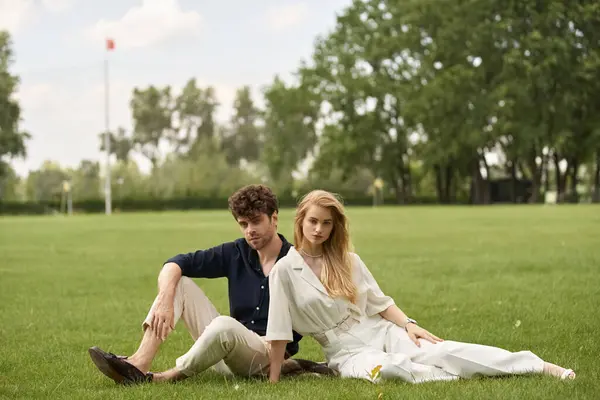 A stylish young couple in elegant attire, relaxing together on the lush green grass of a park. — Stock Photo