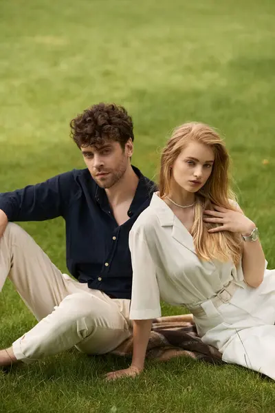 Um casal elegante em trajes elegantes se senta na grama verde, desfrutando uns dos outros empresa em um ambiente ao ar livre sereno. — Fotografia de Stock