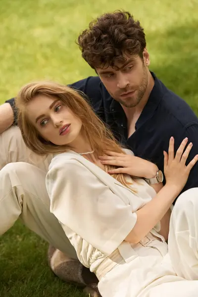 A stylish young couple in elegant attire relaxing together on green grass in a luxurious outdoor setting. — Stock Photo