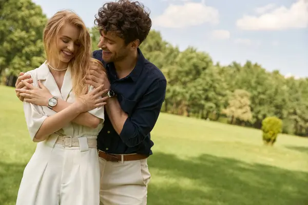 Una bella giovane coppia in elegante abbigliamento che abbraccia teneramente in un campo verde, incarnando amore e serenità. — Foto stock