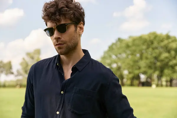 A stylish man in sunglasses stands confidently in a vast field, soaking in the tranquility around him. — Stock Photo