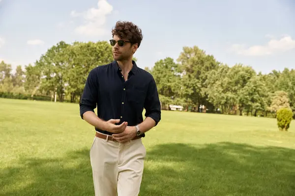 A man in a blue shirt and tan pants enjoys a leisurely walk in a lush green field under the vast open sky. — Stock Photo