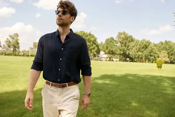 Un hombre con una camisa azul y pantalones bronceados camina con gracia en un campo exuberante. - foto de stock