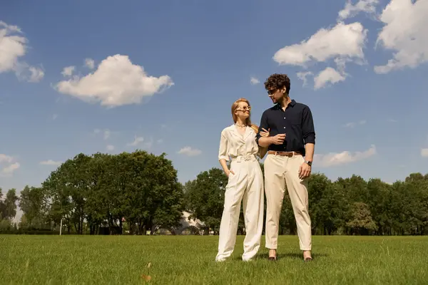 Стильный молодой человек и женщина, одетые в элегантный наряд стоят бок о бок на пышном зеленом поле. — стоковое фото