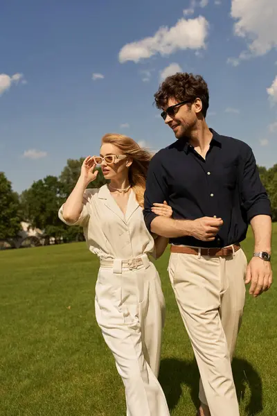A stylish duo, dressed in elegant attire, leisurely walk through a verdant field. — Stock Photo