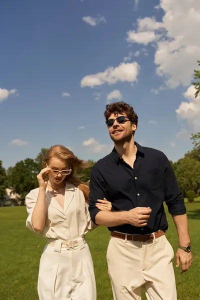 A beautiful young couple in elegant clothing strolls through a green park, embodying an old-money style and luxurious lifestyle. — Stock Photo