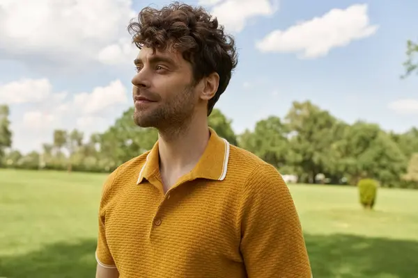 Чоловік, одягнений у яскраво-жовту сорочку, впевнено стоїть у величезному полі, наповненому пишною зеленню під сонцем теплим сяйвом. — стокове фото
