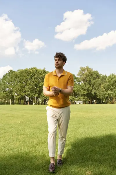 Um homem elegante em uma camisa amarela vibrante fica graciosamente no meio da vegetação exuberante de um campo gramado. — Fotografia de Stock