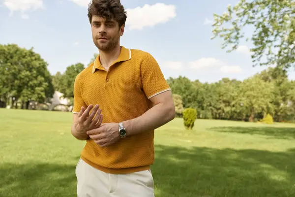 A man in a yellow polo shirt stands confidently in a park, surrounded by lush greenery and enjoying the sunny weather. — Stock Photo