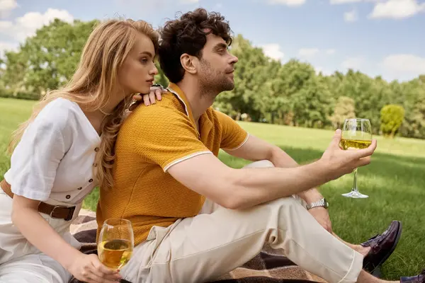 Stylish couple enjoying a romantic picnic in a park, holding wine glasses and immersed in conversation. — стокове фото