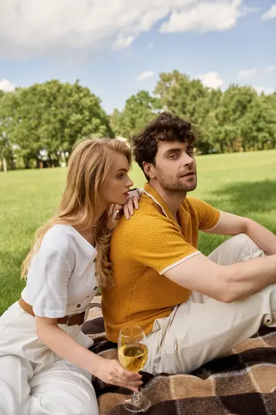 Un jeune couple élégant, élégamment habillé, se détend sur une couverture dans un cadre de parc luxuriant, incarnant un style de vie luxueux. — Photo de stock
