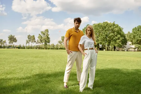 Una bella giovane coppia, vestita elegantemente, in piedi insieme in un lussureggiante campo verde, trasudando un senso di lusso ricco vecchio denaro. — Foto stock