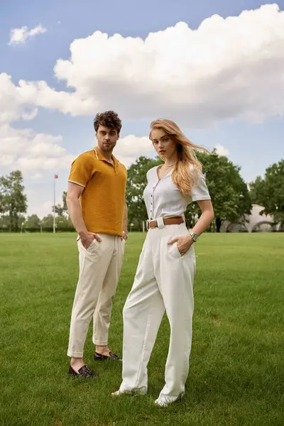 A beautiful young couple, elegantly dressed, standing in a lush green field, embodying a classic and sophisticated lifestyle. — Stock Photo