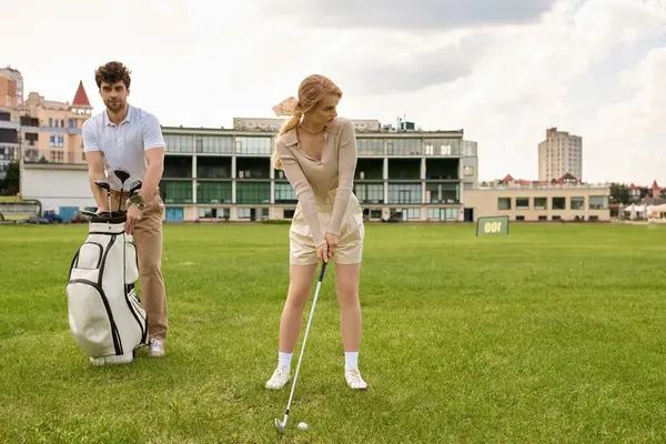 Una giovane coppia, vestita elegantemente, gioca a golf su un campo erboso in un ambiente lussuoso. — Foto stock