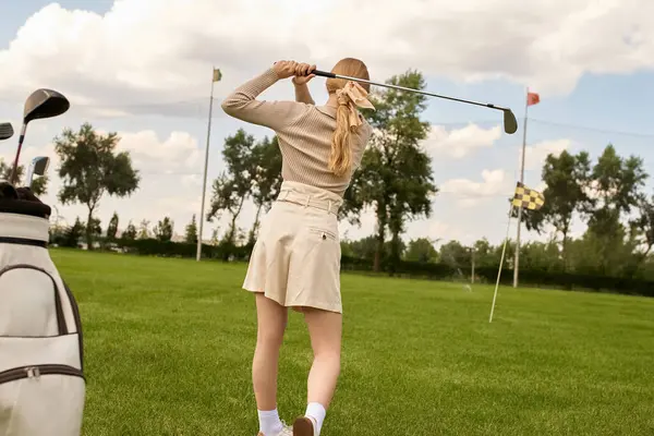 Una donna elegante in abbigliamento elegante oscilla con grazia una mazza da golf in un campo lussureggiante, incarnando uno stile di vita di classe superiore. — Foto stock