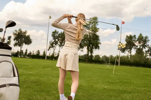 A stylish woman in elegant attire gracefully swings a golf club in a lush field, embodying an upper-class lifestyle. — Stock Photo