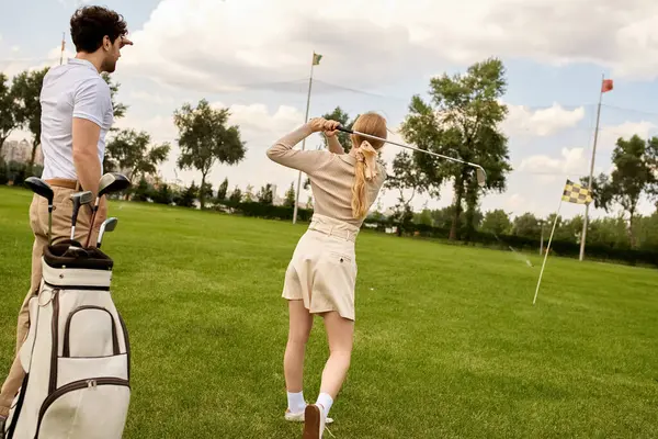 Un uomo e una donna in elegante abbigliamento si divertono a giocare a golf su un rigoglioso campo verde, circondati dalla serenità di un prestigioso golf club. — Foto stock