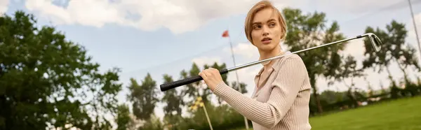Uma jovem mulher em traje elegante habilmente balança um taco de golfe no campo verde durante um passeio de lazer. — Fotografia de Stock