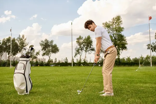 Un homme vêtu de vêtements élégants frappe une balle de golf sur un terrain vert luxuriant dans un club de golf. — Photo de stock