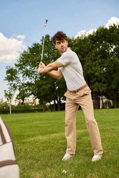 Un giovane in elegante abbigliamento oscilla una mazza da golf su un campo verde, incarnando lo stile di vita di lusso di vecchi soldi. — Foto stock