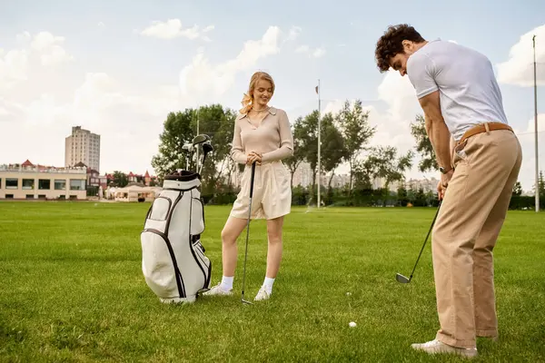 Un uomo e una donna vestiti elegantemente godono di un giro di golf su un campo verde lussureggiante, incarnando uno stile di vita di lusso. — Foto stock