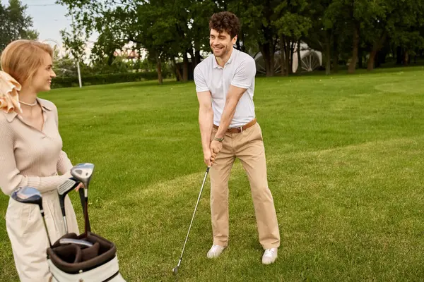 Una giovane coppia, elegantemente vestita, si gode una partita di golf su un lussureggiante campo verde in un prestigioso golf club. — Foto stock