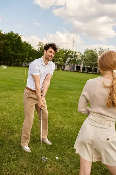 Young couple in elegant attire enjoying a round of golf on a lush green course in a luxurious setting. — Stock Photo