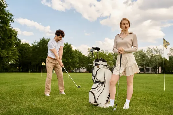 A young couple in elegant attire playing golf on a lush green field at a prestigious club. — стокове фото