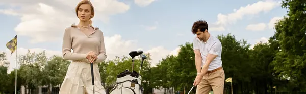 A young couple in stylish attire plays a round of golf in a park, enjoying a leisurely day together on the green. — Stock Photo