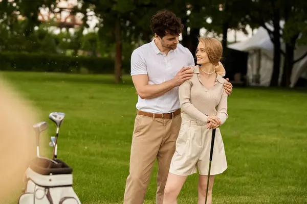 Um jovem casal elegante em traje elegante de pé lado a lado em um campo de golfe verde exuberante. — Fotografia de Stock