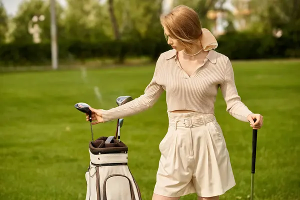 Una giovane donna elegantemente tiene una borsa da golf su un campo verde in un golf club, godendo di una piacevole giornata all'aria aperta. — Foto stock