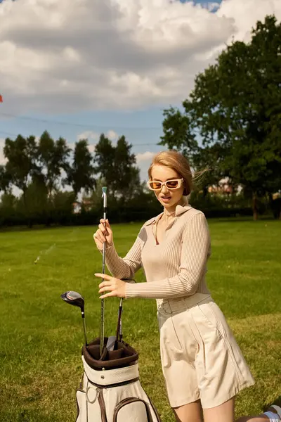 Uma jovem mulher em traje elegante com seu clube de golfe em um cenário exuberante parque. — Fotografia de Stock