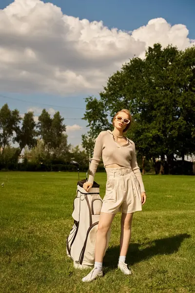 Una giovane donna sofisticata si trova con grazia in un campo con una borsa da golf, godendo l'aria aperta con un'aria di raffinata eleganza. — Foto stock