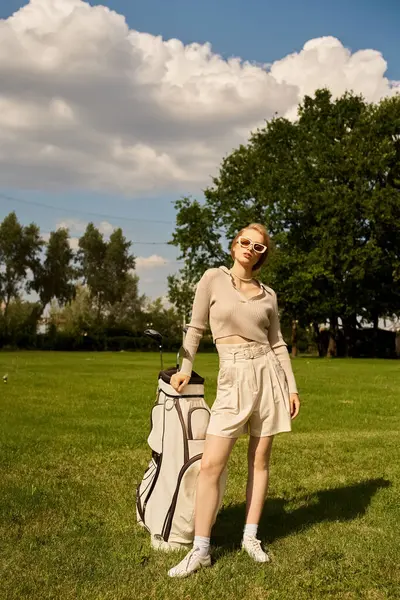 A sophisticated young woman stands gracefully in a field with a golf bag, enjoying the outdoors with an air of refined elegance. — Stock Photo
