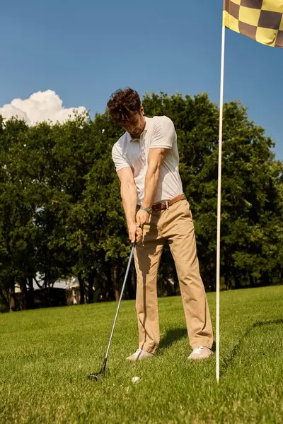A man in elegant attire swings a golf club, hitting a ball on a grassy field at a golf club. — Stock Photo