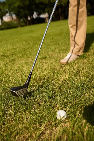 Un uomo in abiti eleganti si prepara a tee off su un campo verde in una mazza da golf, incarnando vecchio stile di denaro e stile di vita della classe superiore. — Foto stock