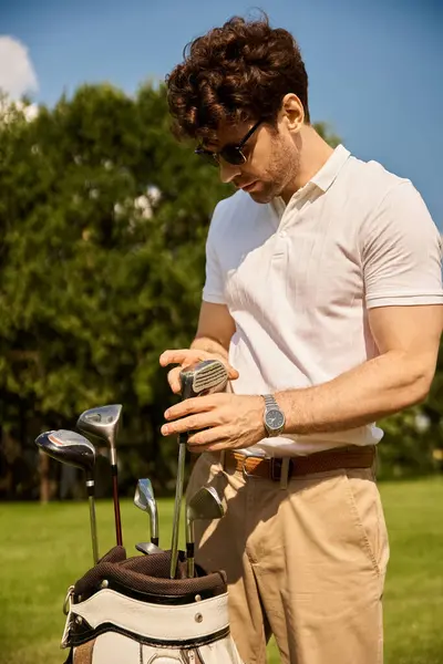 Um homem com roupas elegantes colocando cuidadosamente seus tacos de golfe em um saco em um campo verde em um clube de golfe. — Fotografia de Stock