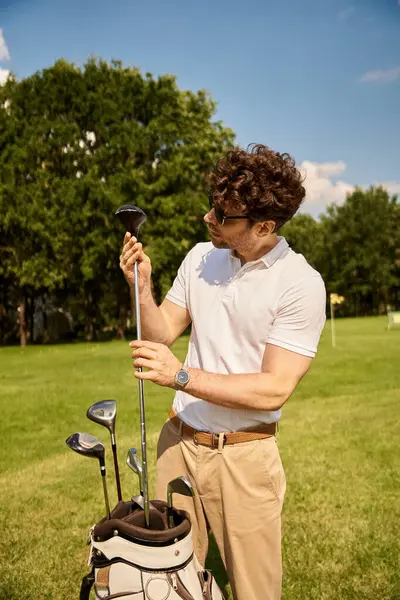 Un hombre elegante con ropa elegante sostiene una bolsa de golf en un campo verde exuberante en un prestigioso club de golf, que encarna el ocio de clase alta. - foto de stock