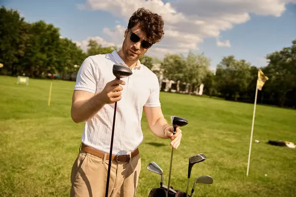 Stylish man in elegant clothing stands outdoors, confidently holding a golf club in his hands on a lush green field. — Stock Photo