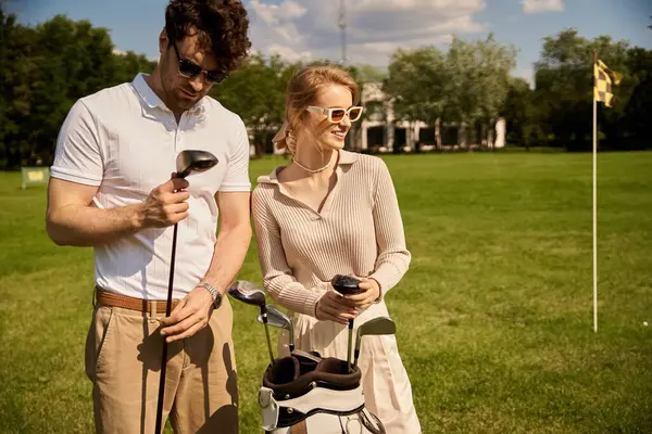 Ein junges Paar, elegant gekleidet, steht gemeinsam auf einem malerischen Golfplatz und verkörpert einen klassischen, großbürgerlichen Lebensstil.. — Stockfoto