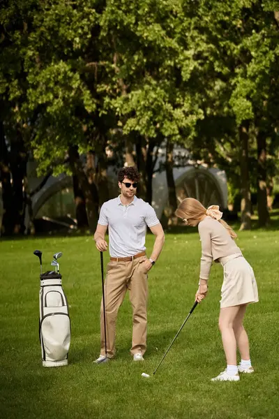 Una giovane coppia vestita in elegante abbigliamento gioca a golf in un lussureggiante parco verde. — Foto stock