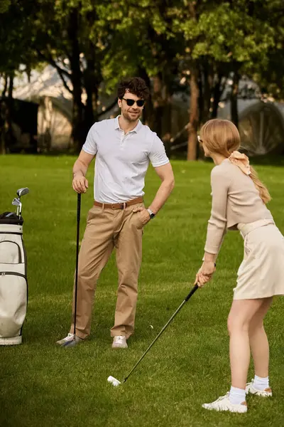 Un giovane uomo e una giovane donna giocano elegantemente a golf in un parco, incarnando lusso e raffinatezza nel loro abbigliamento e altalene.. — Foto stock