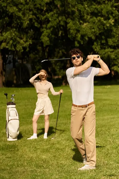 Una giovane coppia vestita in elegante abbigliamento gioca a golf su un lussureggiante campo verde in un parco, godendo di una piacevole giornata all'aria aperta. — Foto stock