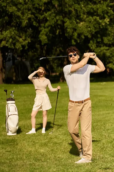 A young couple dressed in elegant attire playing golf on a lush green field in a park, enjoying a leisurely day outdoors. — Stock Photo