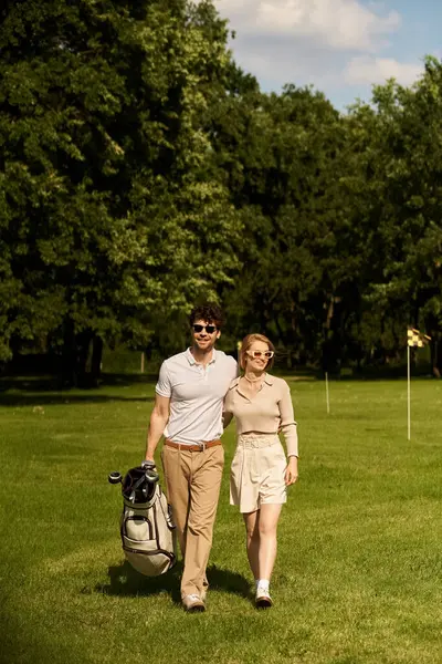 A graceful young couple in elegant attire enjoying a leisurely walk on a picturesque golf course surrounded by lush greenery. — стокове фото