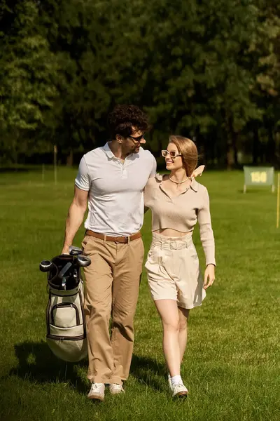 A sophisticated young couple in elegant attire walking on a luxurious golf course, enjoying a leisurely afternoon together. — стокове фото