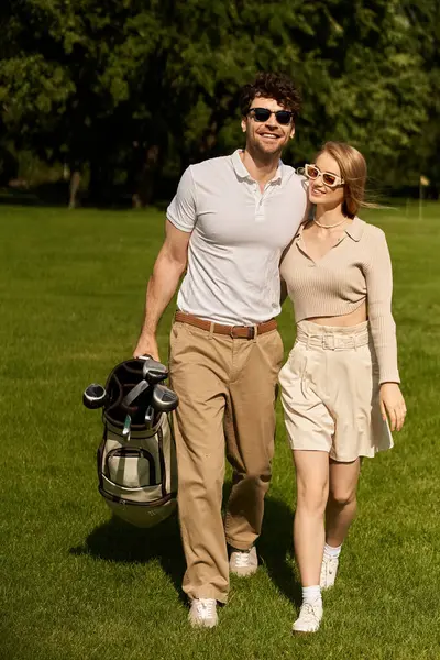 A young couple in elegant attire leisurely walking across a luxurious golf course on a sunny day. — стокове фото