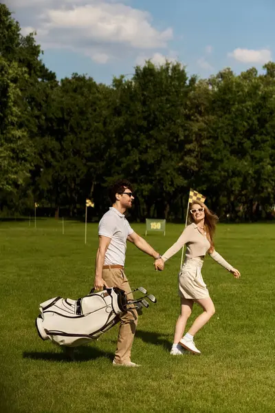 A stylish young couple, dressed elegantly, walk hand in hand through a lush golf course in a display of classic sophistication. — Stock Photo